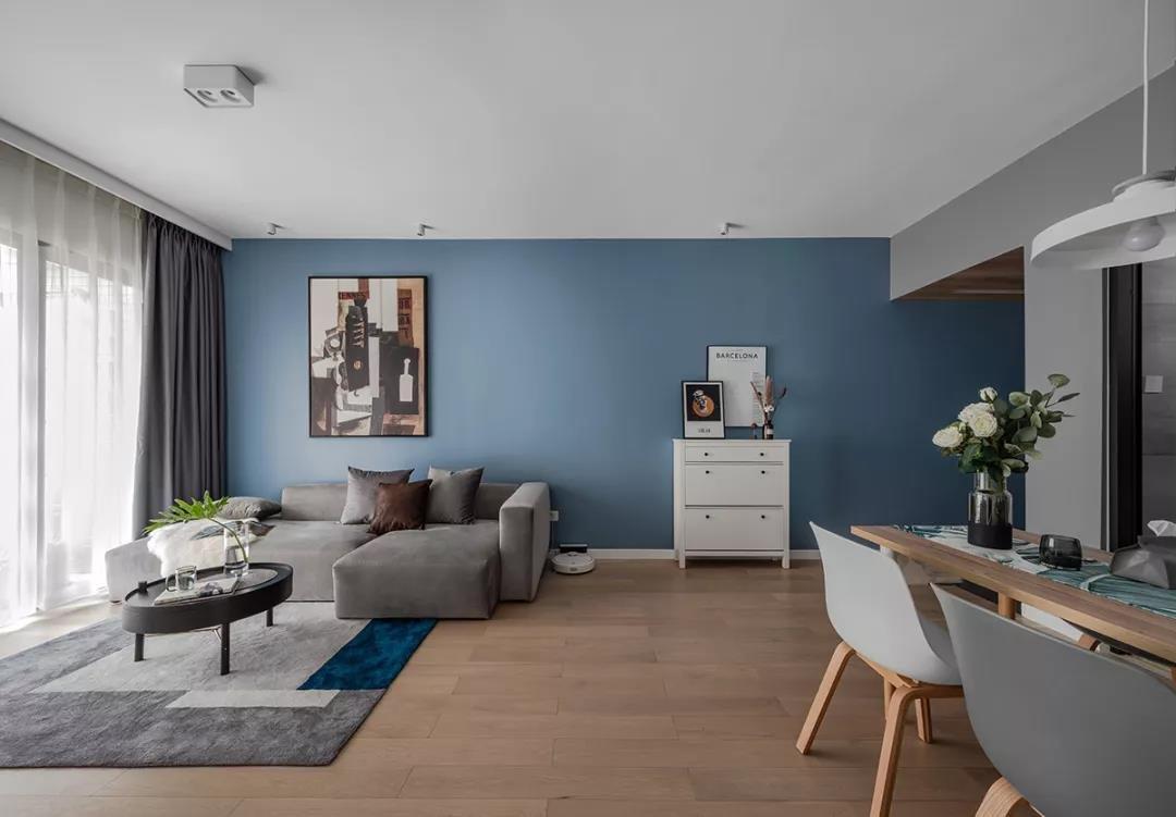 装修设计图蓝色的沙发墙贯穿到玄关，挂上一大幅画，结合灰色布艺沙发，地面还垫着简约灰色的地毯，沙发侧边还有个小斗柜，整体空间设计显得安静优雅好舒适客厅在灰色电视墙+蓝